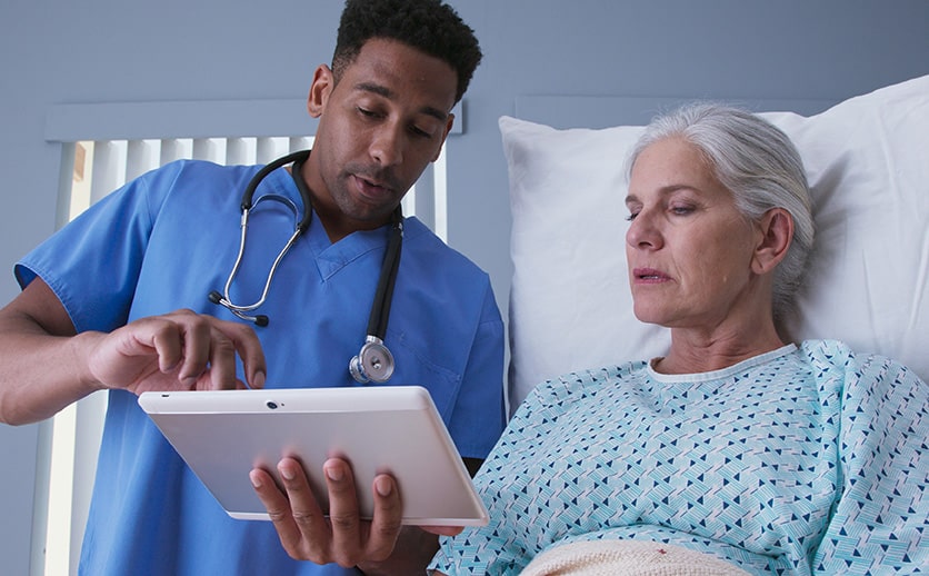 RN and senior patient looking at tablet computer at hospital.