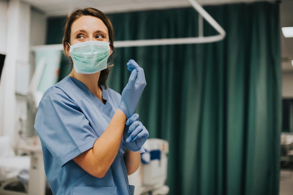 Nurse putting on gloves in hospital room